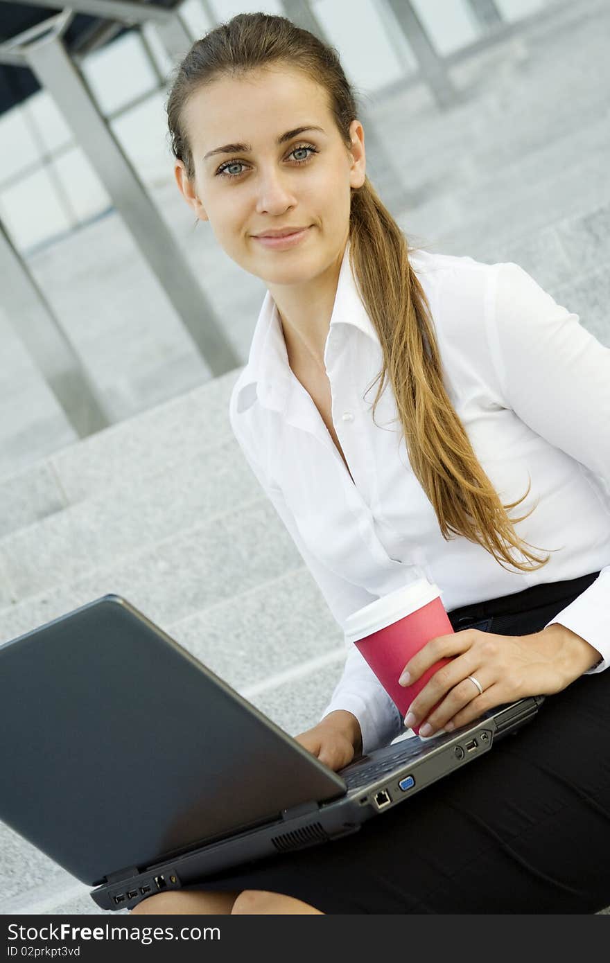 Young, beautiful woman business over coffee in the fresh air sitting on the stairs, office building, on my knees your laptop. Young, beautiful woman business over coffee in the fresh air sitting on the stairs, office building, on my knees your laptop