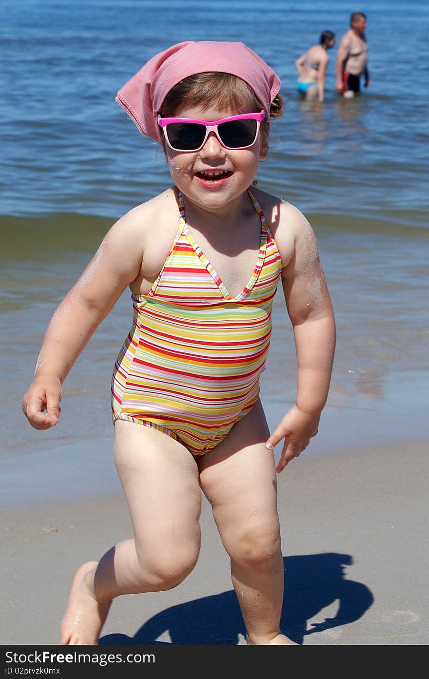 Little girl in pink glasses, runs along the beach