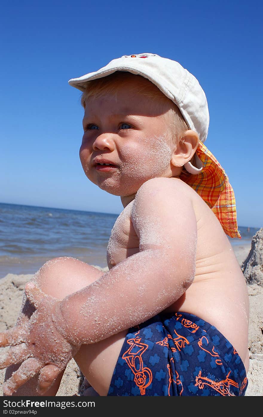 Small boy sits on beach, it is looked on sea