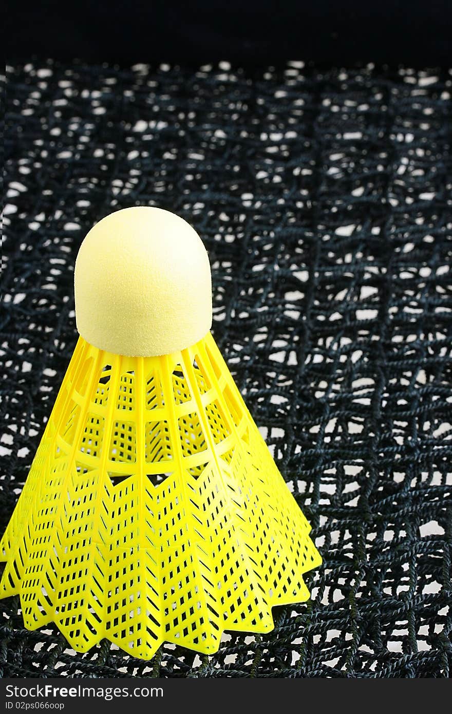 A bright yellow badminton shuttlecock on a black badminton net. A bright yellow badminton shuttlecock on a black badminton net.