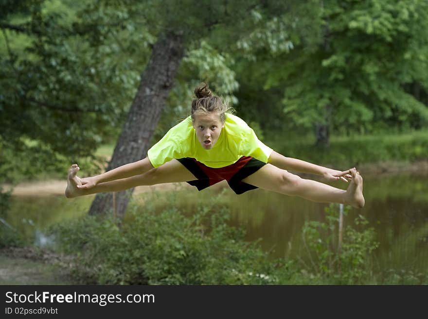 Cute young girl jumping outside in front of pond. Cute young girl jumping outside in front of pond