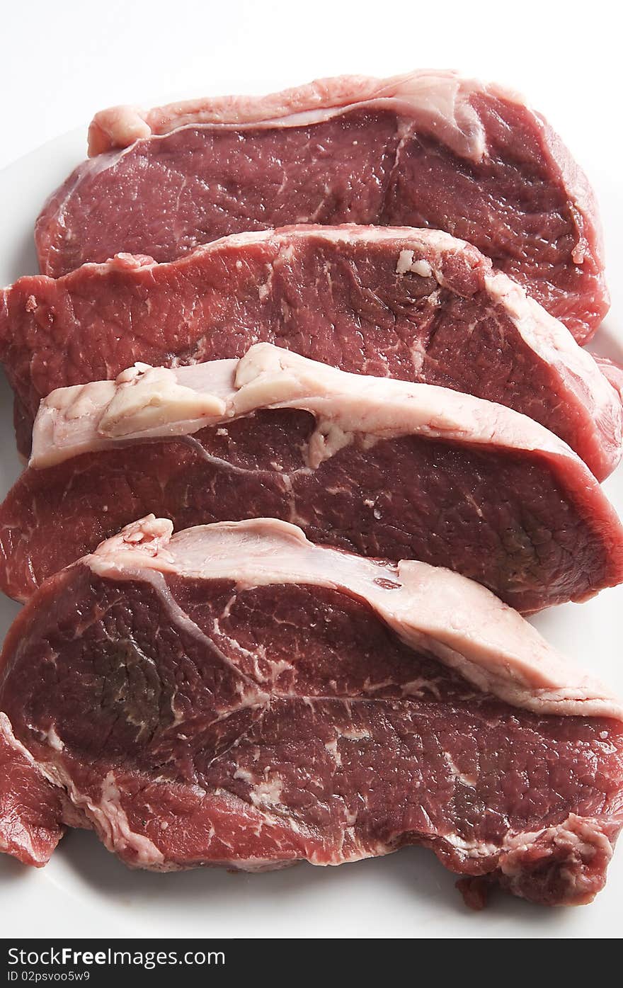 Four red raw steaks on a white plate, ready for the frying pan