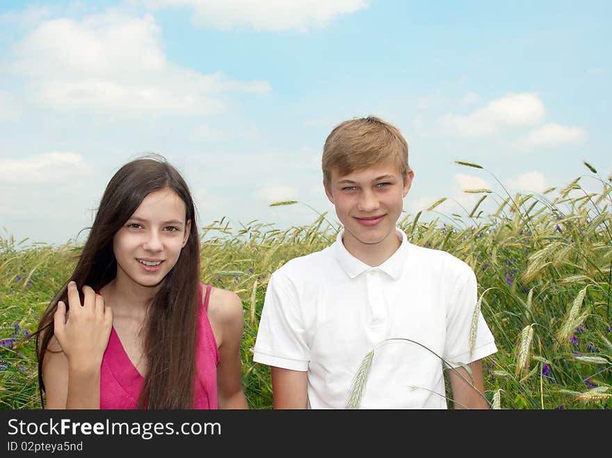 Smiling girl and boy standing in a field on background of blue sky with clouds