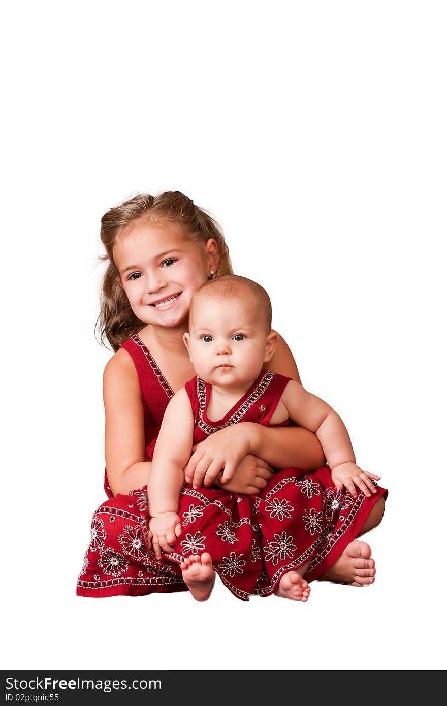 Big sister holding little sister wearing matching dresses. White background