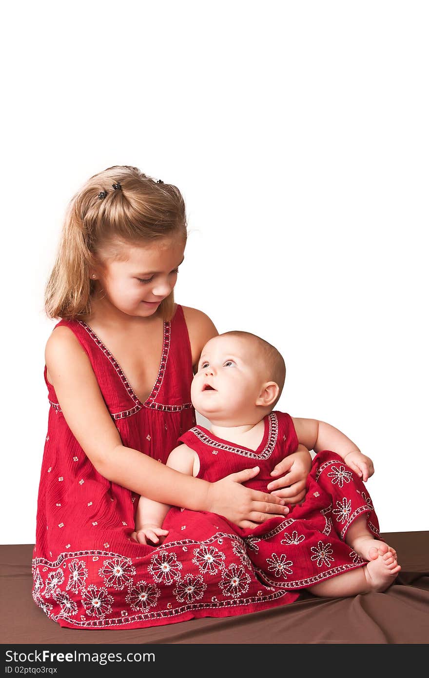 Big sister holding little sister wearing matching dresses.  White background