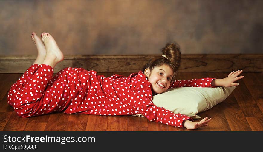 A happy preteen laying on a wood flloor with her pillow in polka-dot pajamas. A happy preteen laying on a wood flloor with her pillow in polka-dot pajamas.