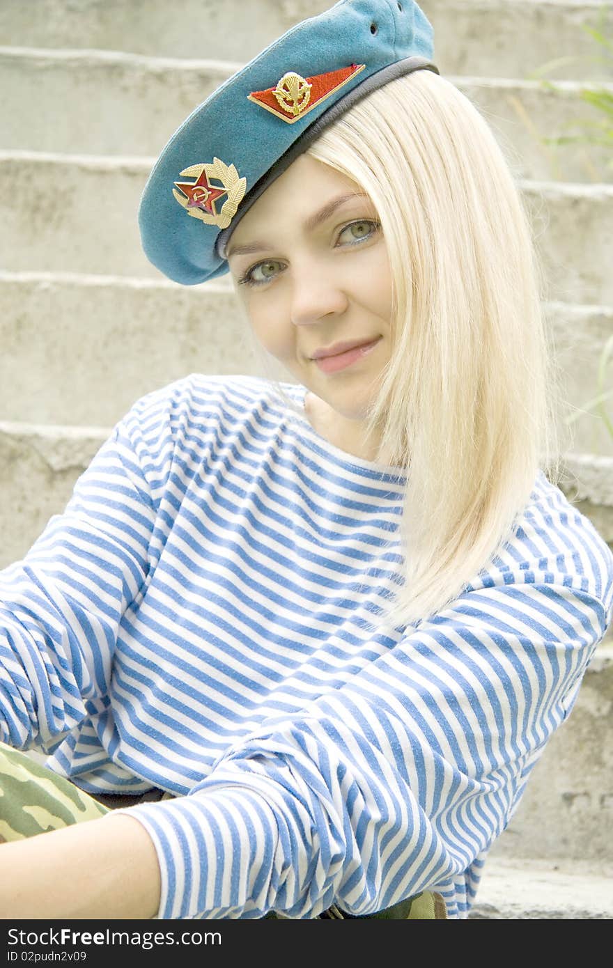 Woman with green eyes in the military form sits on a ladder. Woman with green eyes in the military form sits on a ladder