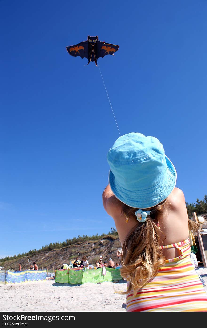 A little girl in a blue cap, it sets a kite on the beach