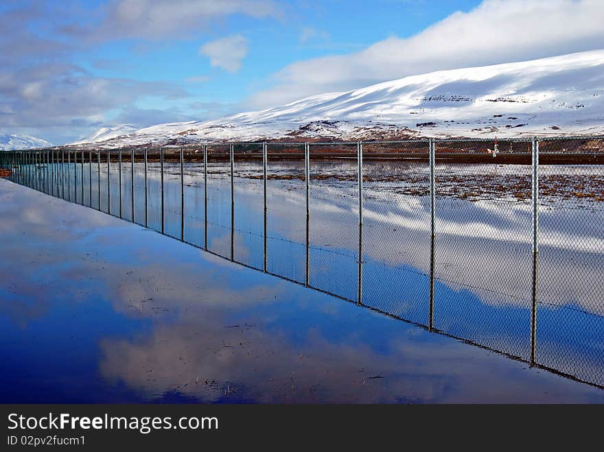 A fence and a blue sky mirrors in a water. A fence and a blue sky mirrors in a water.