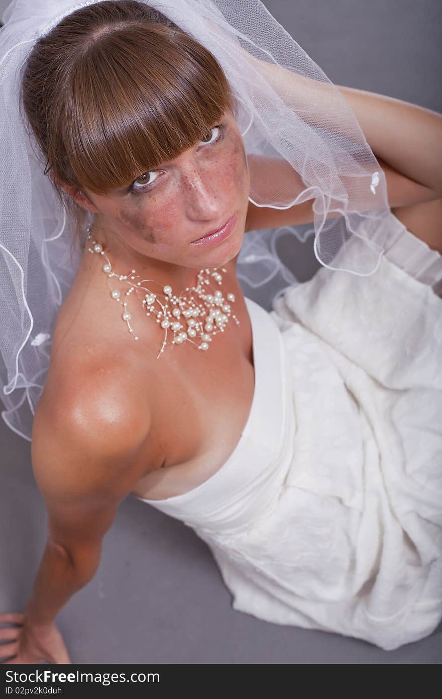 Sad bride crying on the ground over grey background. Sad bride crying on the ground over grey background