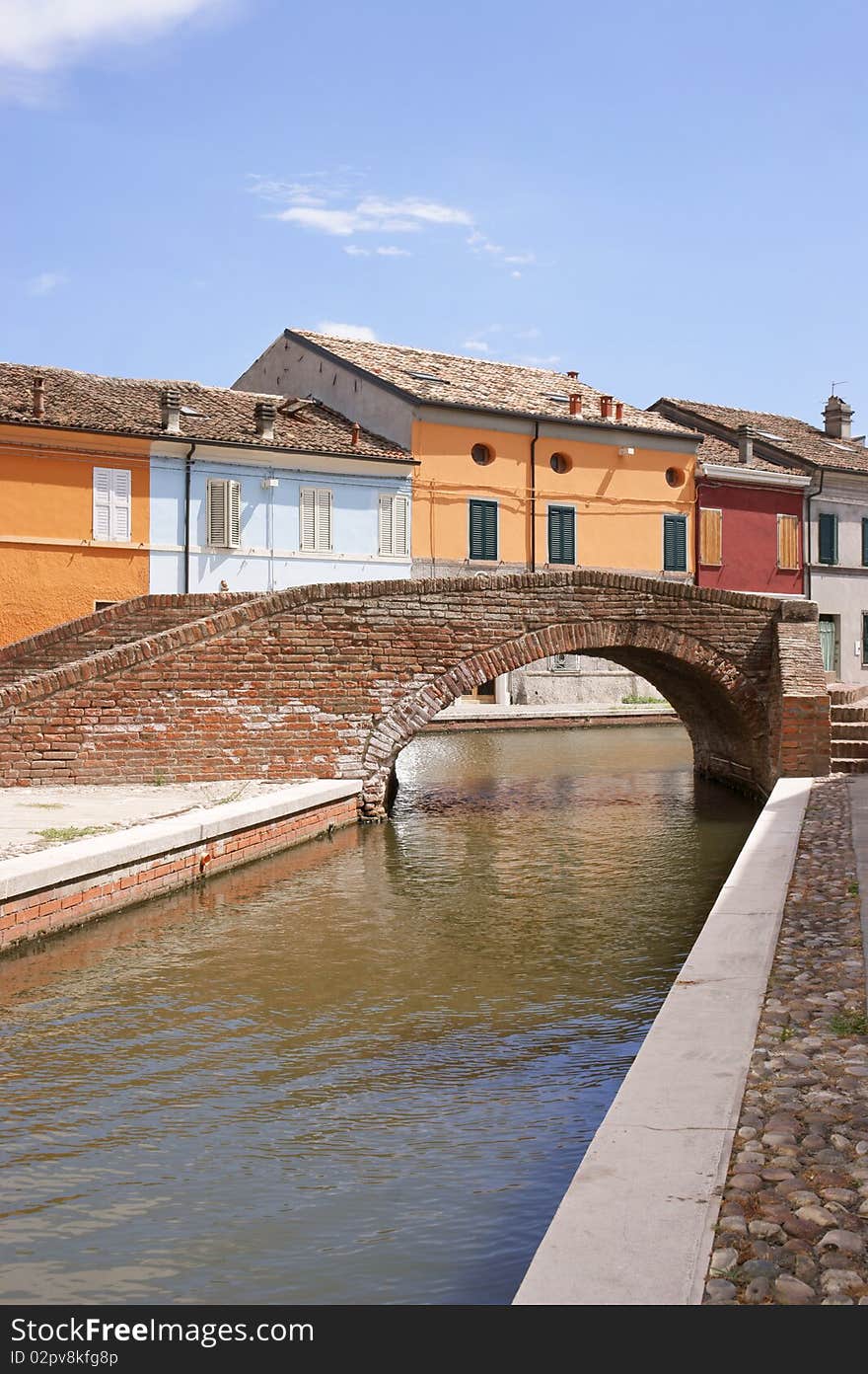 Stone arch bridge over a canal with colored houses behind