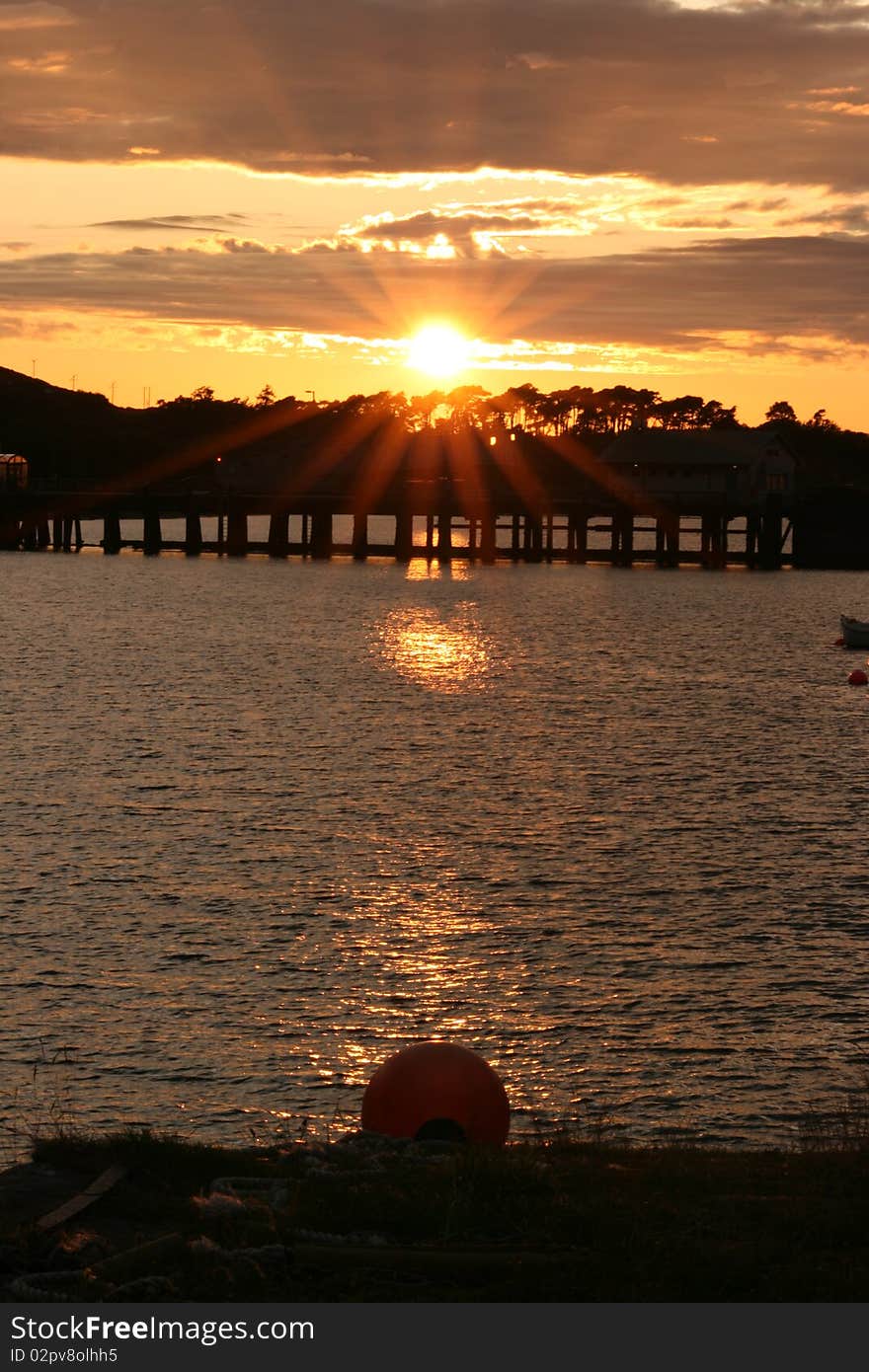 Sunset over the water on the Isle of Mull in Scotland with silhouette of trees and pier in distance. Sunset over the water on the Isle of Mull in Scotland with silhouette of trees and pier in distance.