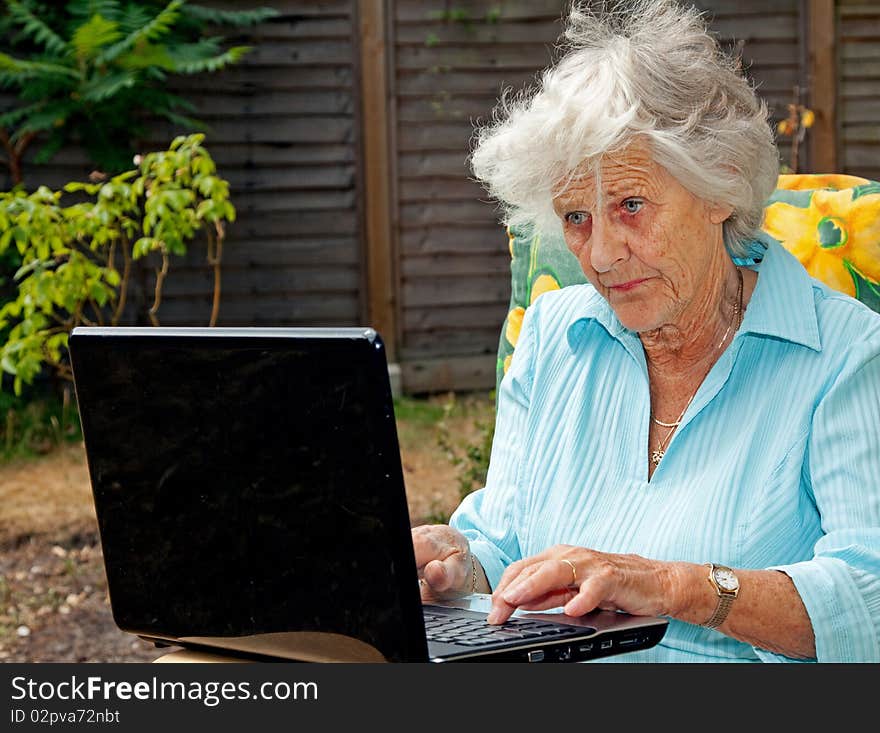 A senior woman using a laptop computer in her garden. A senior woman using a laptop computer in her garden