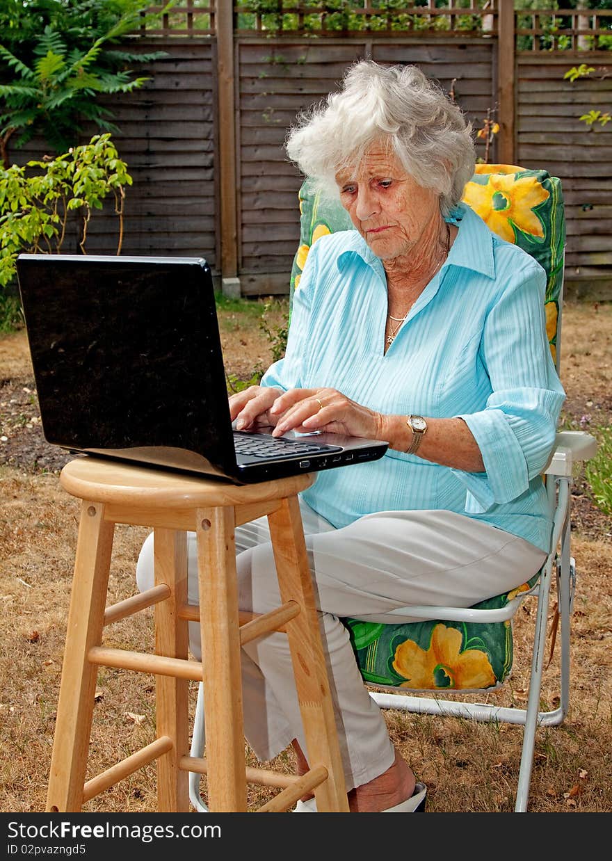 A senior woman using a laptop computer in her garden. A senior woman using a laptop computer in her garden