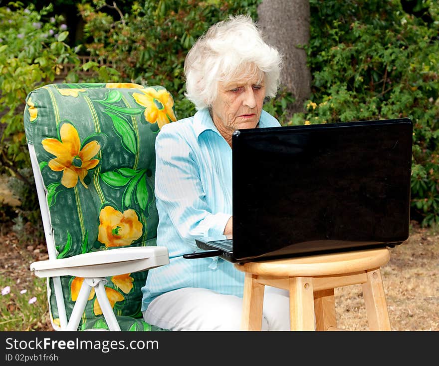 A senior woman using a laptop computer in her garden. A senior woman using a laptop computer in her garden