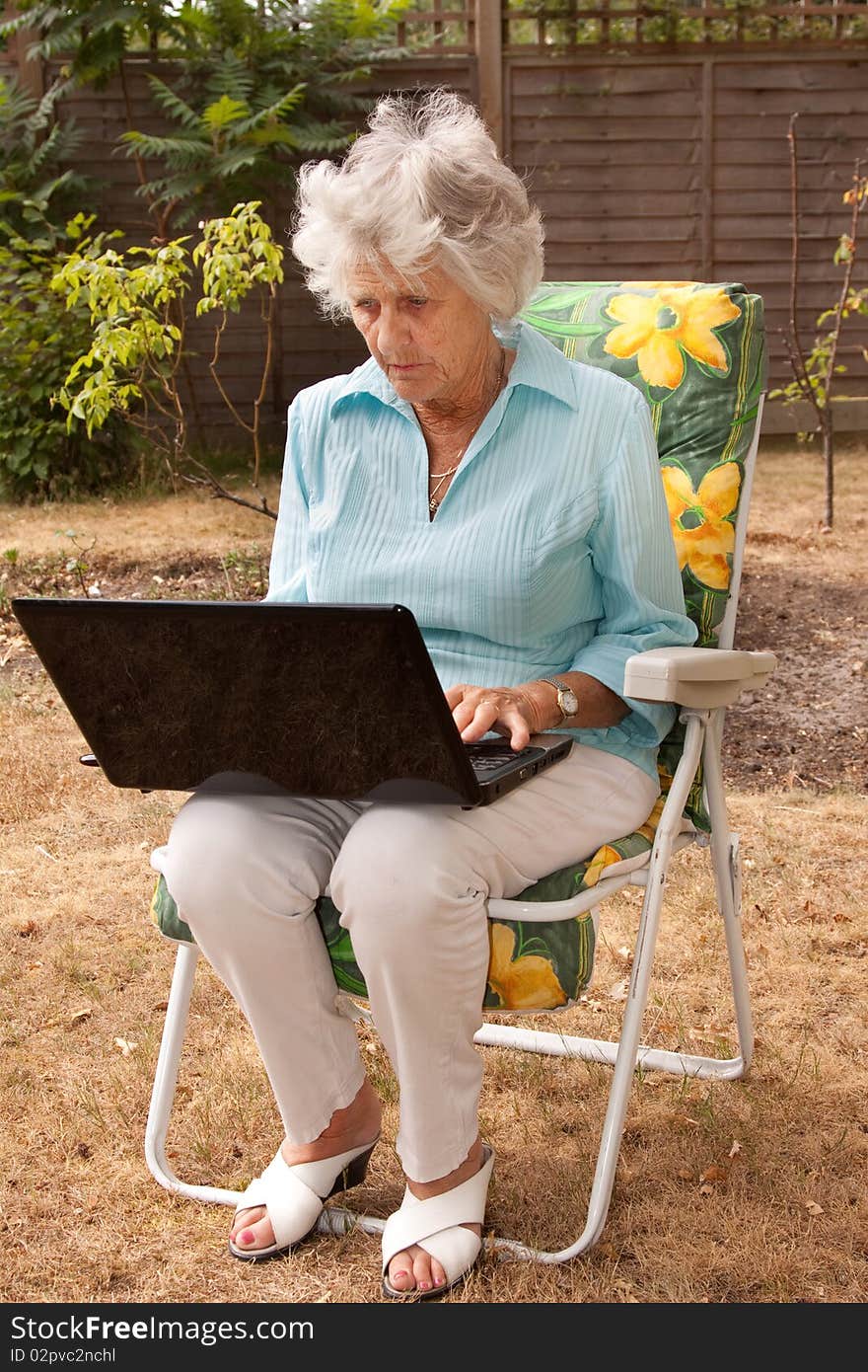 A senior woman using a laptop computer in her garden. A senior woman using a laptop computer in her garden