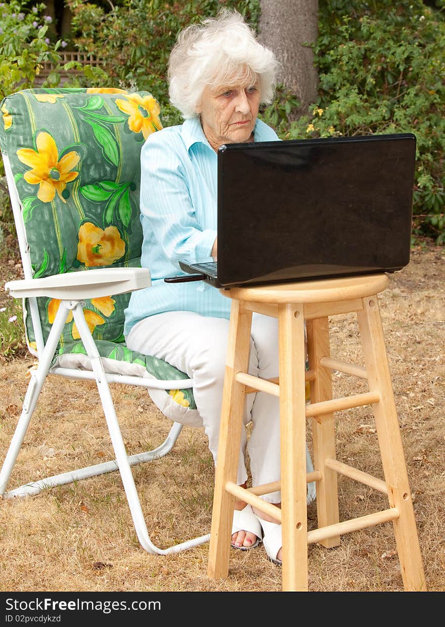 An elderly woman using a laptop computer in her garden. An elderly woman using a laptop computer in her garden