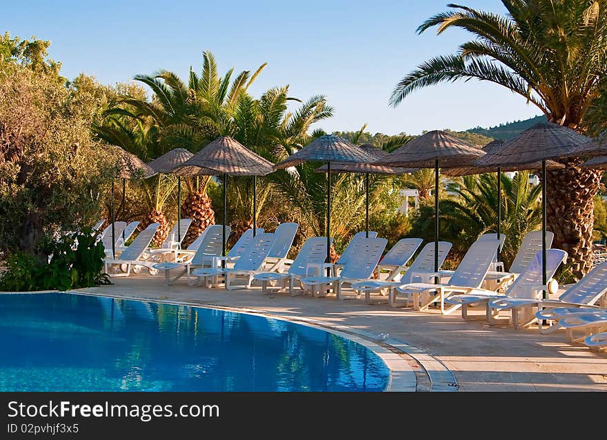 The row of chaise longues under beach umbrellas near the swimming pool. The row of chaise longues under beach umbrellas near the swimming pool