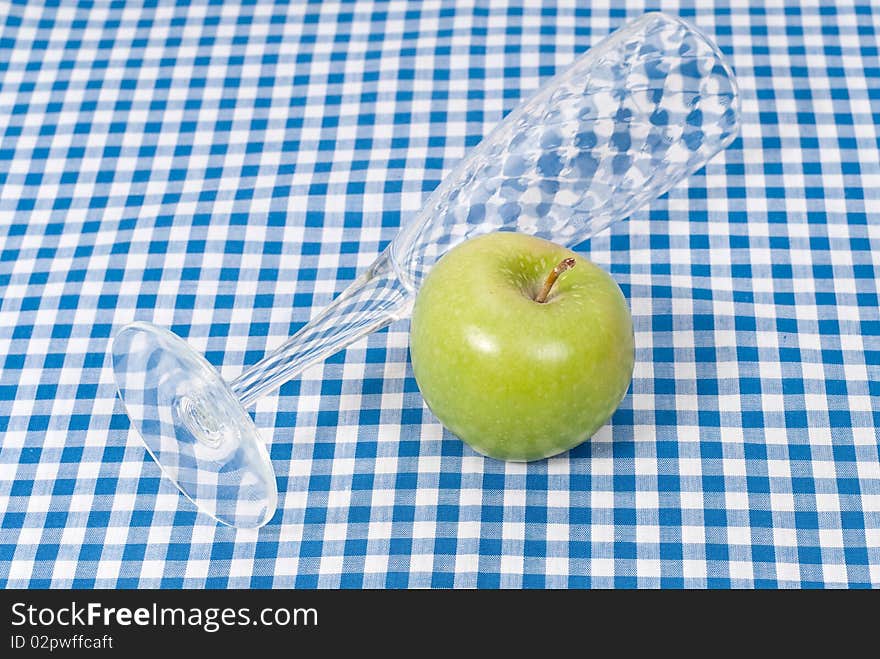 A green apple with a flute glass on picnic cloth. A green apple with a flute glass on picnic cloth