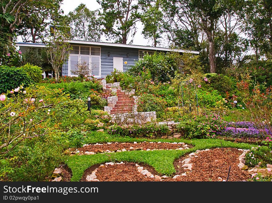 Log cabin in flower garden of park with stone staircase. Log cabin in flower garden of park with stone staircase.