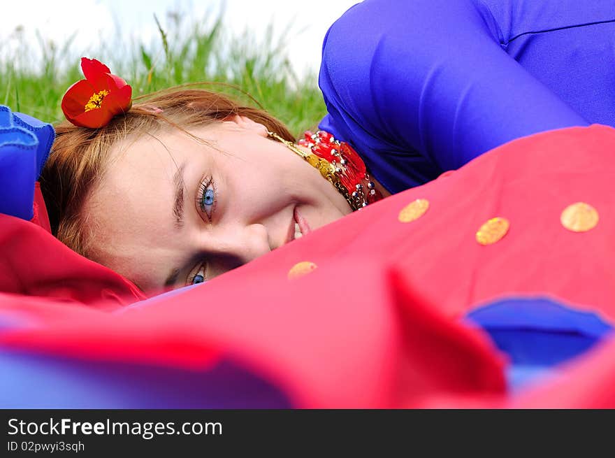 Gipsy girl in blue, lying on green grass with a flower