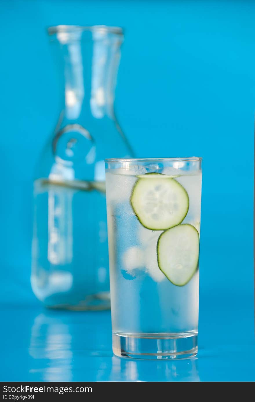 Ice water with cucumbers on blue in front of glass carafe. Ice water with cucumbers on blue in front of glass carafe