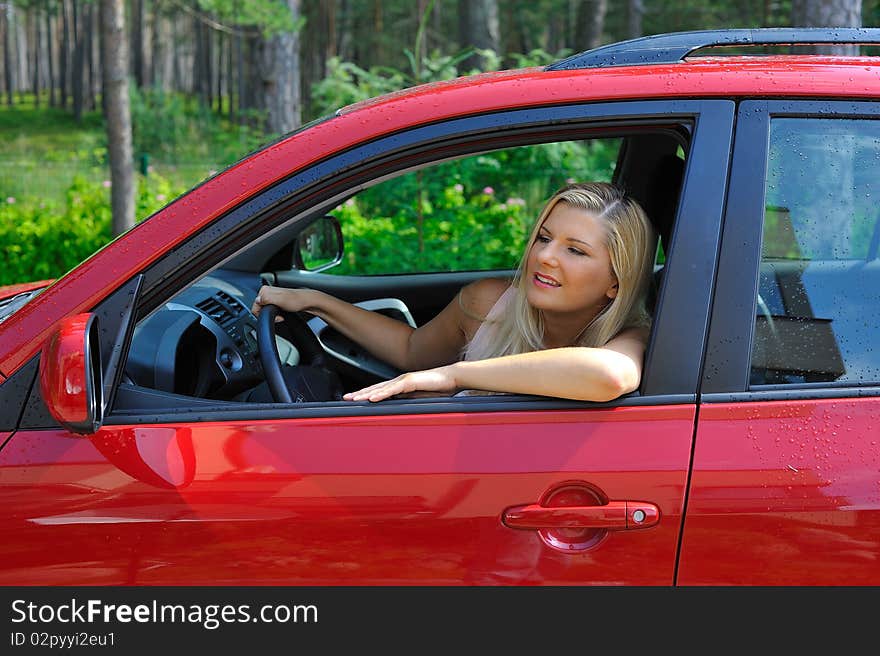 Beautiful woman driver in red shiny car outdoors smiling