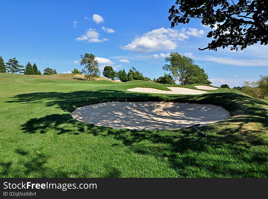 A series of bunkers on a golf course in mid-summer with one in the shade. A series of bunkers on a golf course in mid-summer with one in the shade