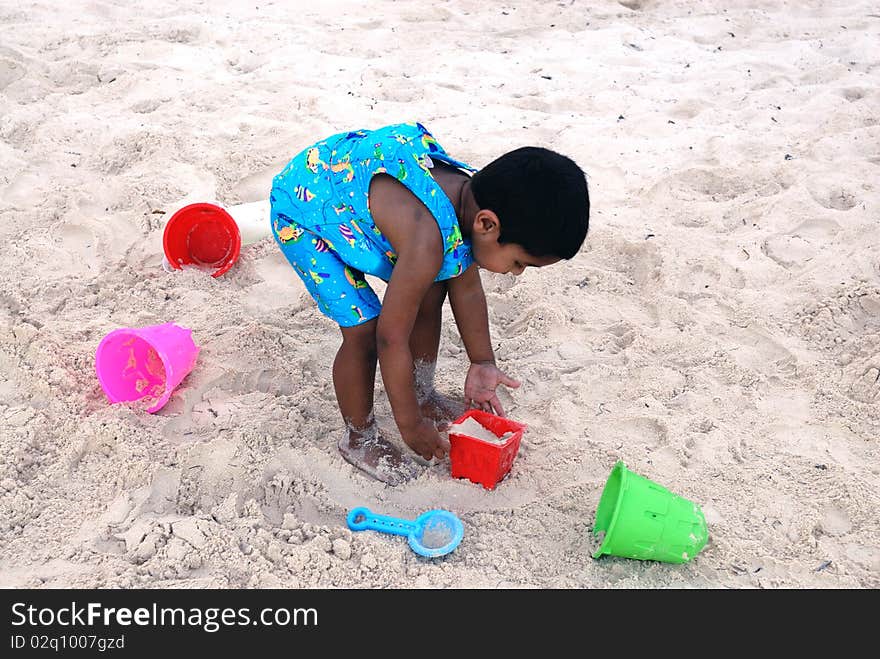 An handsome Indian kid playing with sand at a tropical beach