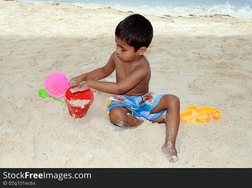 An handsome Indian kid playing with sand at a tropical beach