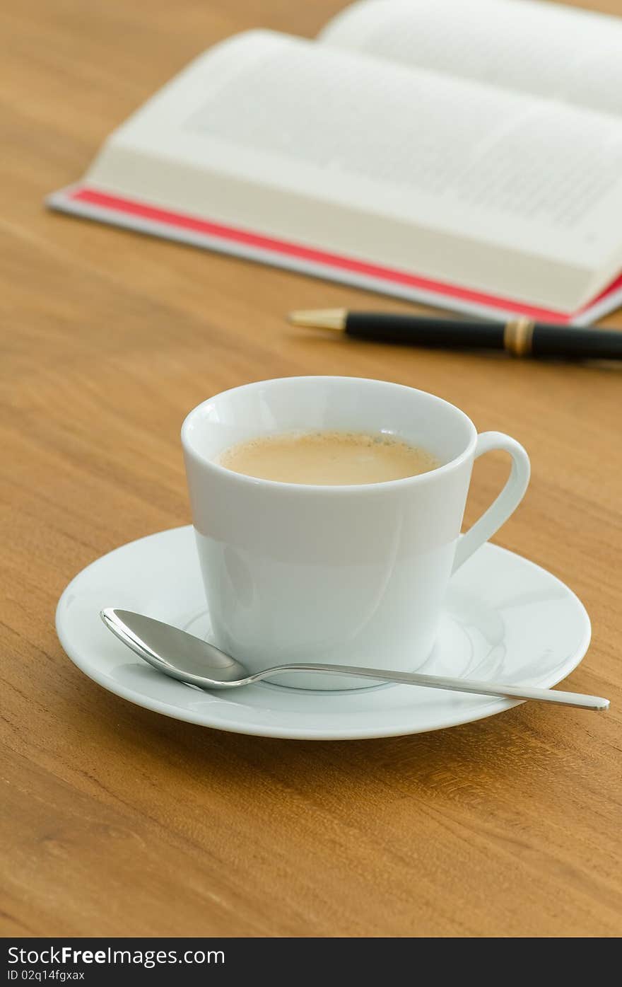 White coffee cup with open book and pen on a wooden table. White coffee cup with open book and pen on a wooden table