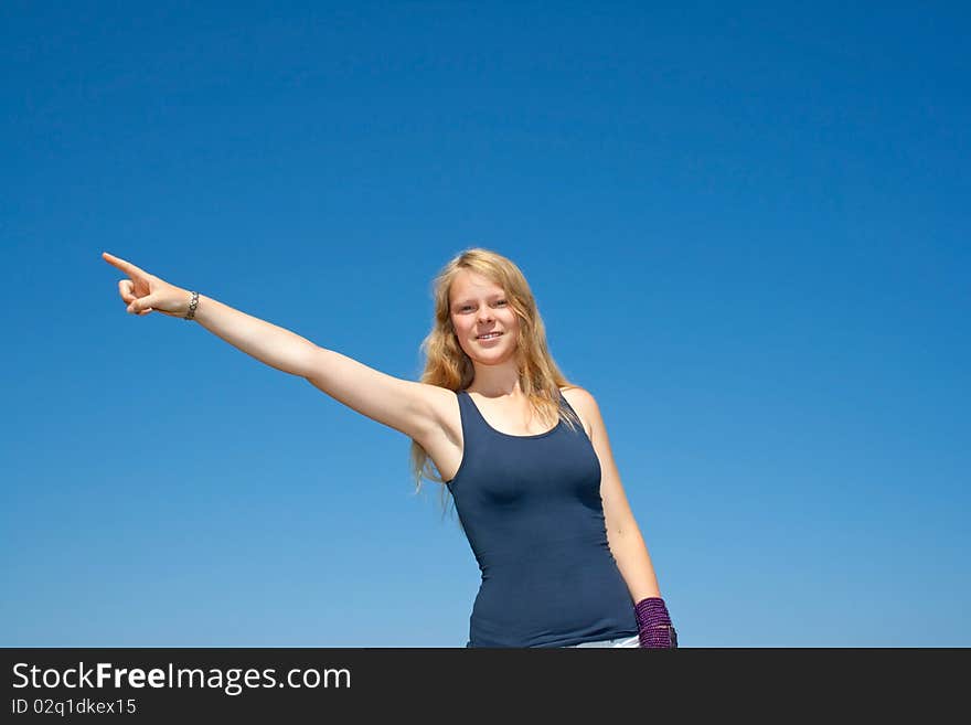 Pretty lady points to the left side, standing in front of blue sky