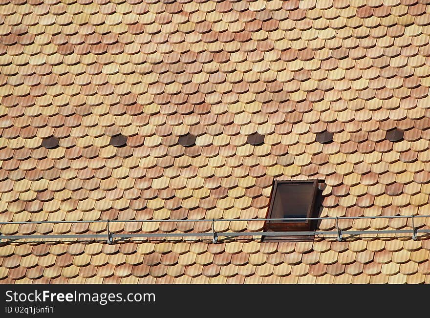 Lots of brown tiles and a window on a roof. Lots of brown tiles and a window on a roof