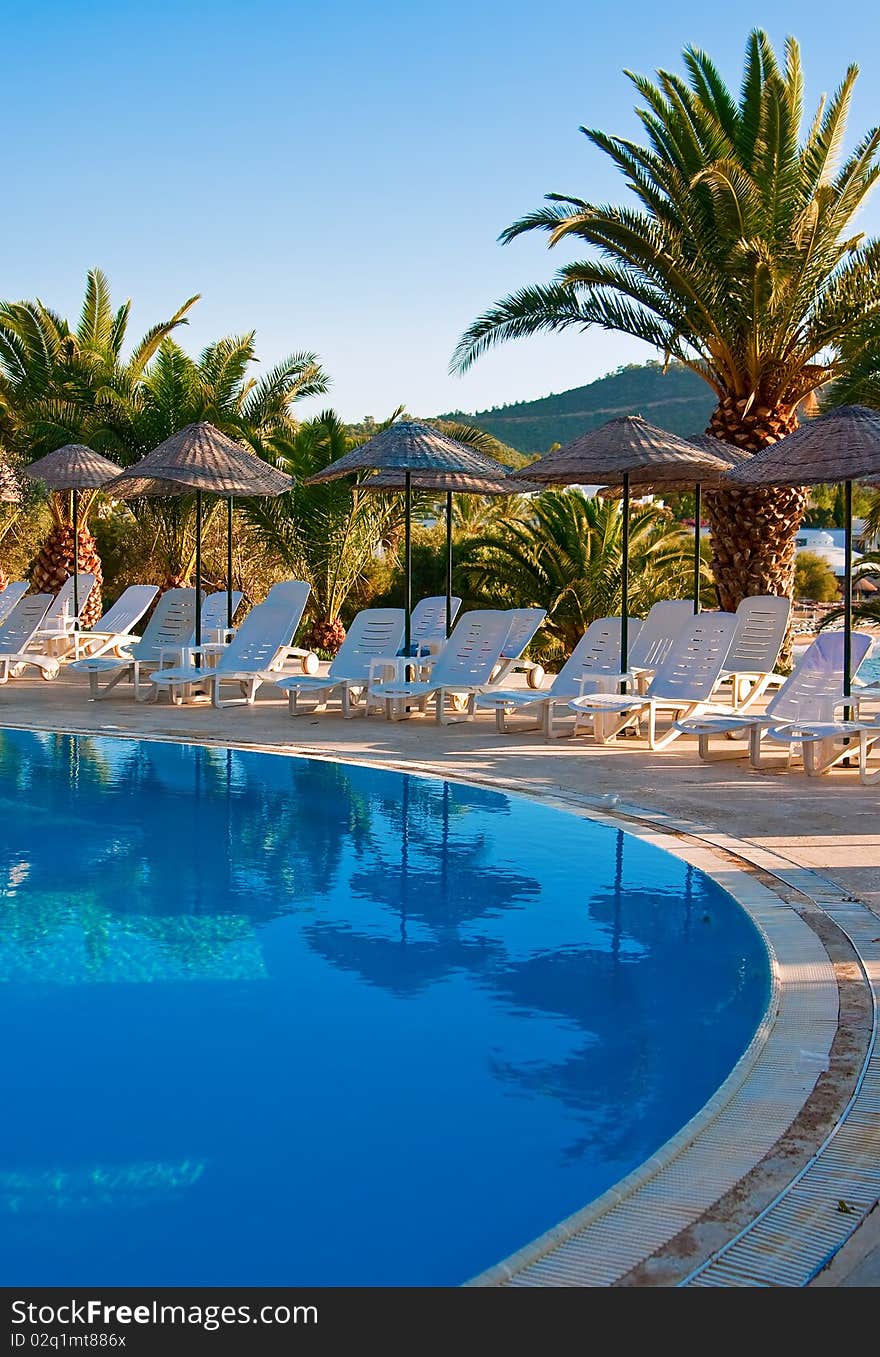 The row of chaise longues under beach umbrellas near the swimming pool. The row of chaise longues under beach umbrellas near the swimming pool