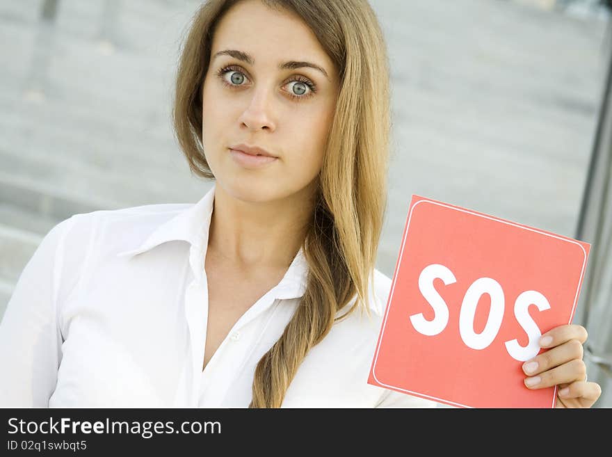 Business woman on a background of office space in the hands holding a red card with the text of SOS. Prayer in aid. Business woman on a background of office space in the hands holding a red card with the text of SOS. Prayer in aid