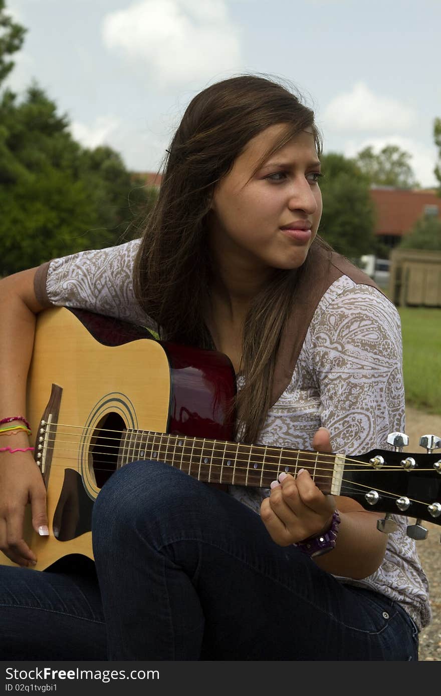 A pretty girl sitting outside playing an acoustic guitar gazes off into the distance. A pretty girl sitting outside playing an acoustic guitar gazes off into the distance.