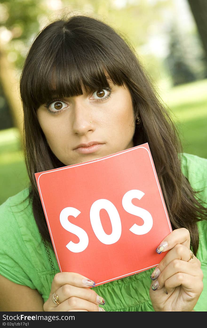 Young woman outdoors in the park holding a red card with the text of SOS. Prayer in aid. Young woman outdoors in the park holding a red card with the text of SOS. Prayer in aid