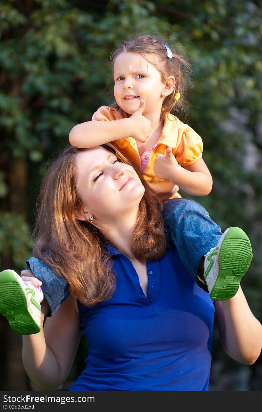 Happy young girl give a thumbs-up while sitting on her mother's shoulders. Happy young girl give a thumbs-up while sitting on her mother's shoulders