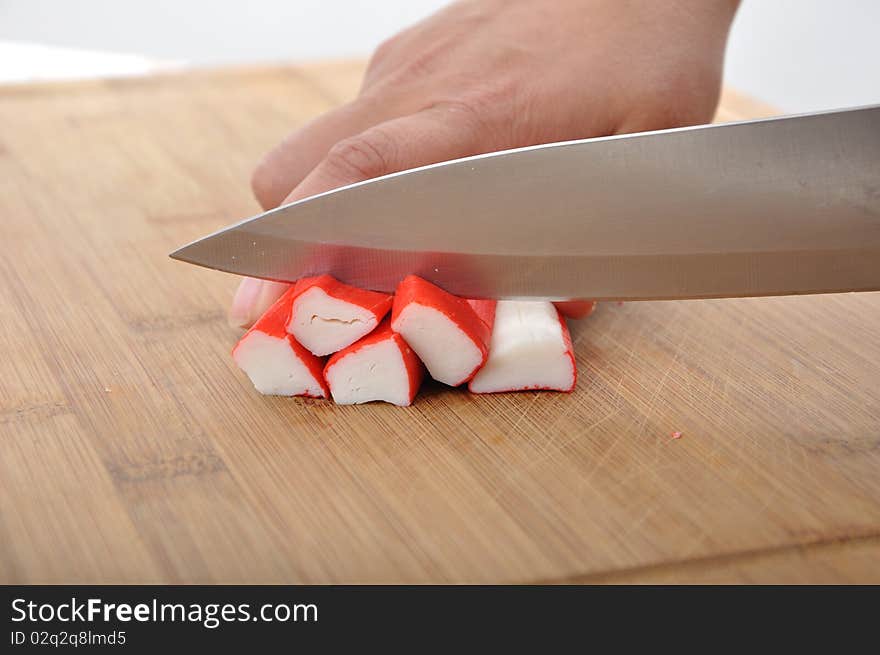 Woman cut pile of surimi on wood desk. Woman cut pile of surimi on wood desk