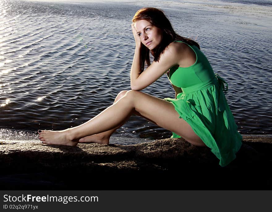 A beautiful young woman sitting on an islet in a green sundress. A beautiful young woman sitting on an islet in a green sundress.