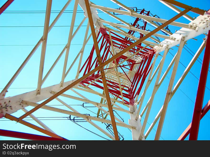 Top of the red and white high voltage electricity pylon against the blue sky. Top of the red and white high voltage electricity pylon against the blue sky