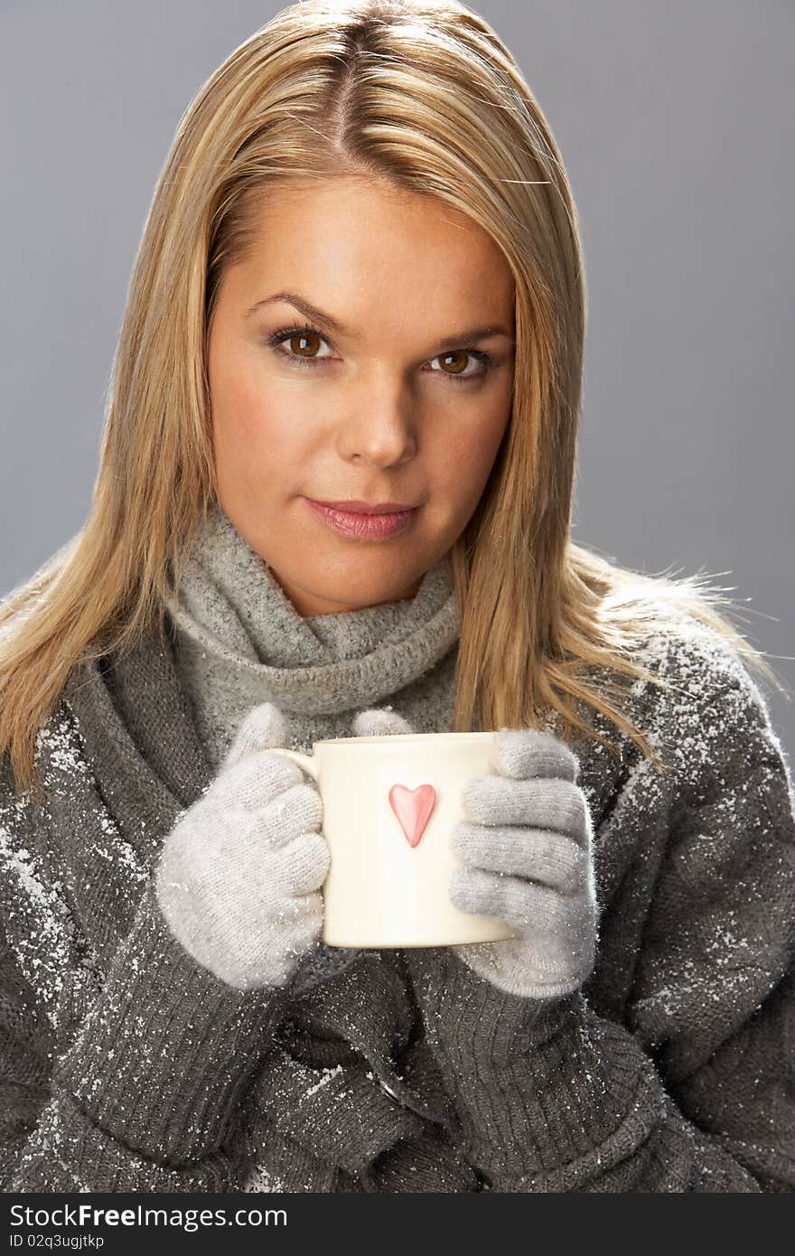 Young Woman Drinking Hot Drink Wearing Knitwear In Studio In Front Of Christmas Tree