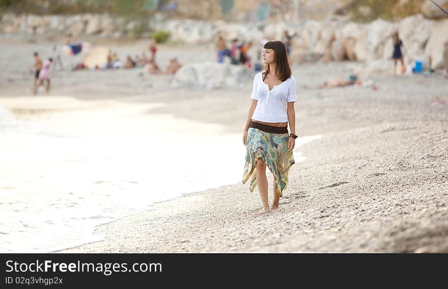 Young beautiful lone girl walking on a crowded beach. Young beautiful lone girl walking on a crowded beach.