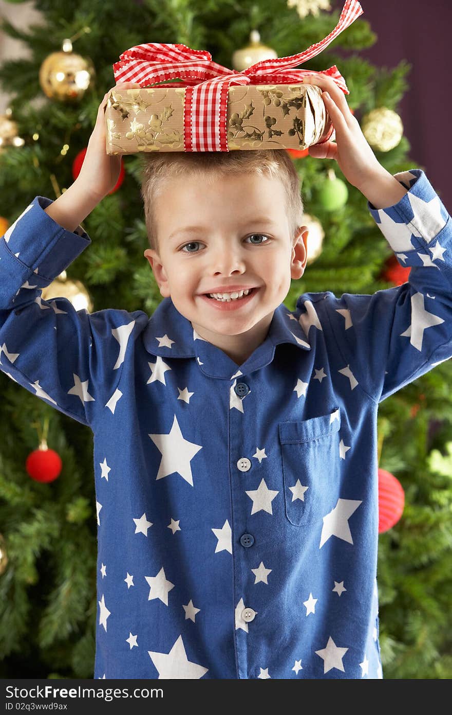 Young Boy Holding Wrapped Present In Front Of Christmas Tree. Young Boy Holding Wrapped Present In Front Of Christmas Tree