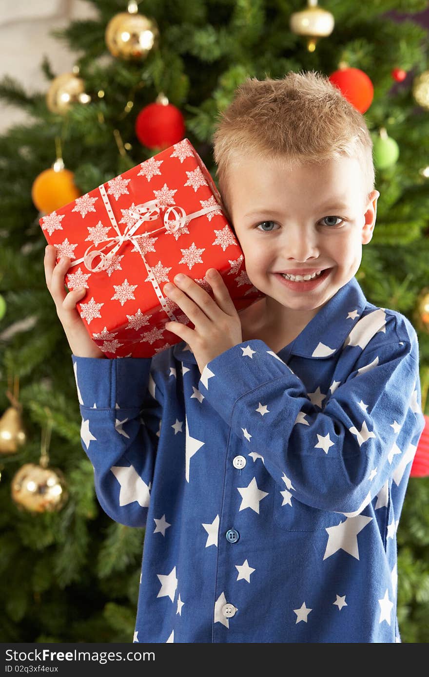 Young Boy Holding Wrapped Present In Front Of Christmas Tree. Young Boy Holding Wrapped Present In Front Of Christmas Tree