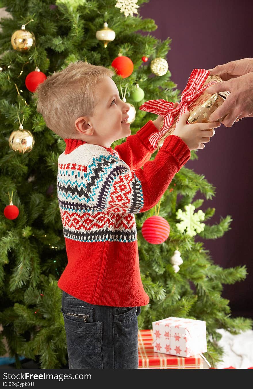 Young Boy Holding Christmas Present In Front Of Christmas Tree. Young Boy Holding Christmas Present In Front Of Christmas Tree