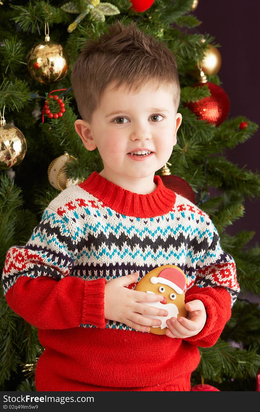 Boy Eating Cookie In Front Of Christmas Tree