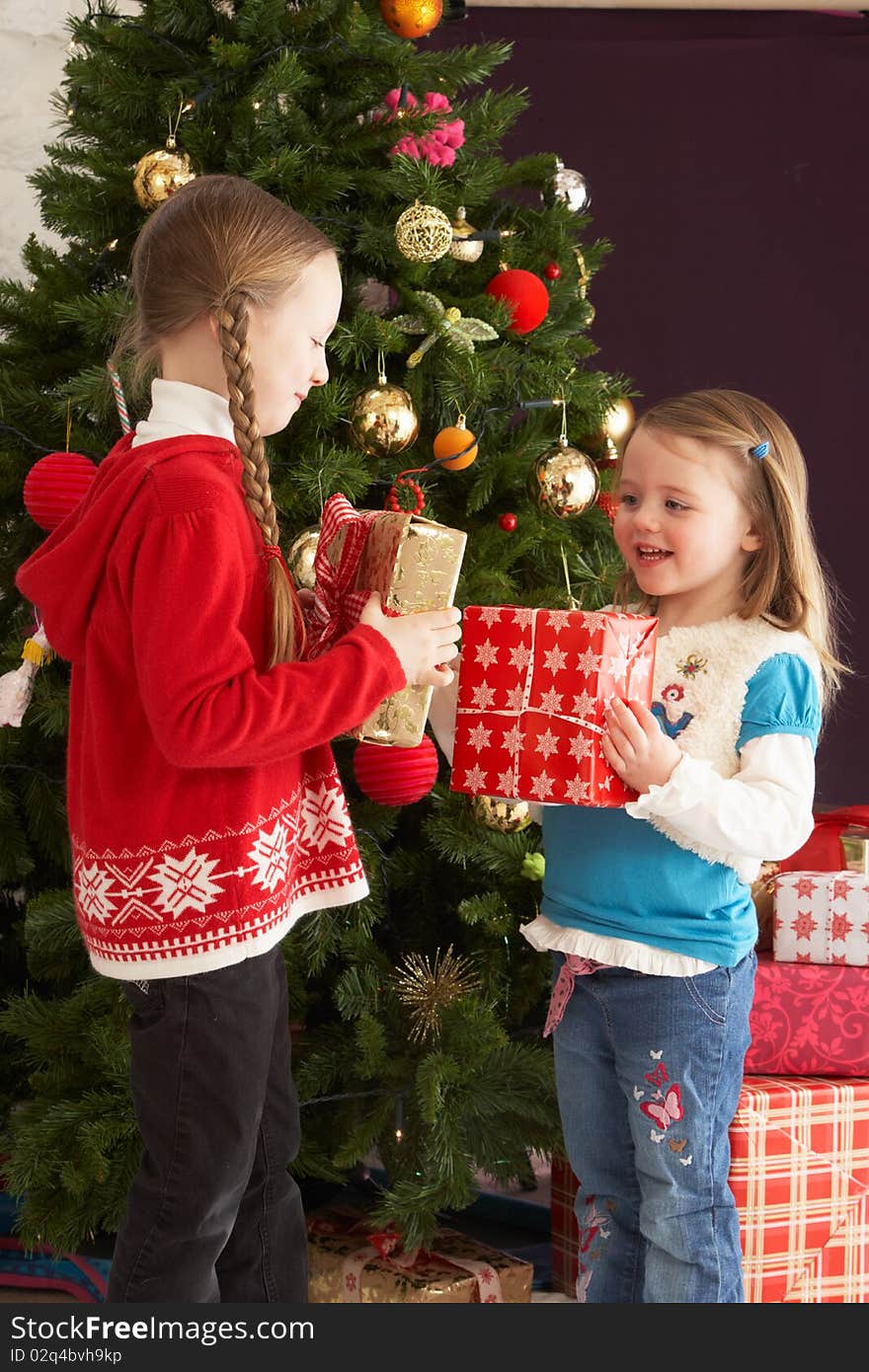 Two Young Girls With Presents In Front Of Tree