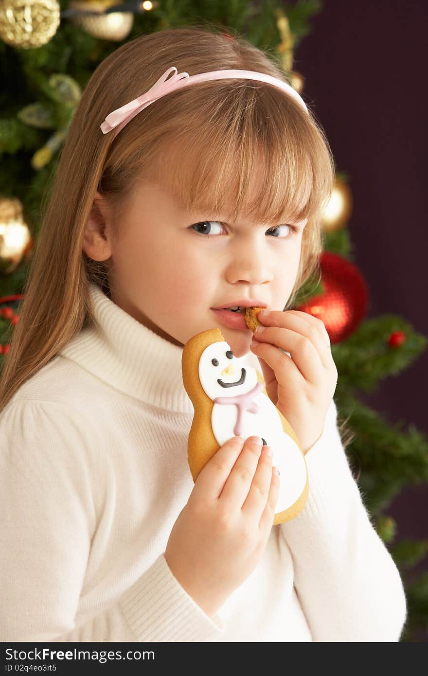 Young Girl Eating Cookie In Front Of Christmas Tree