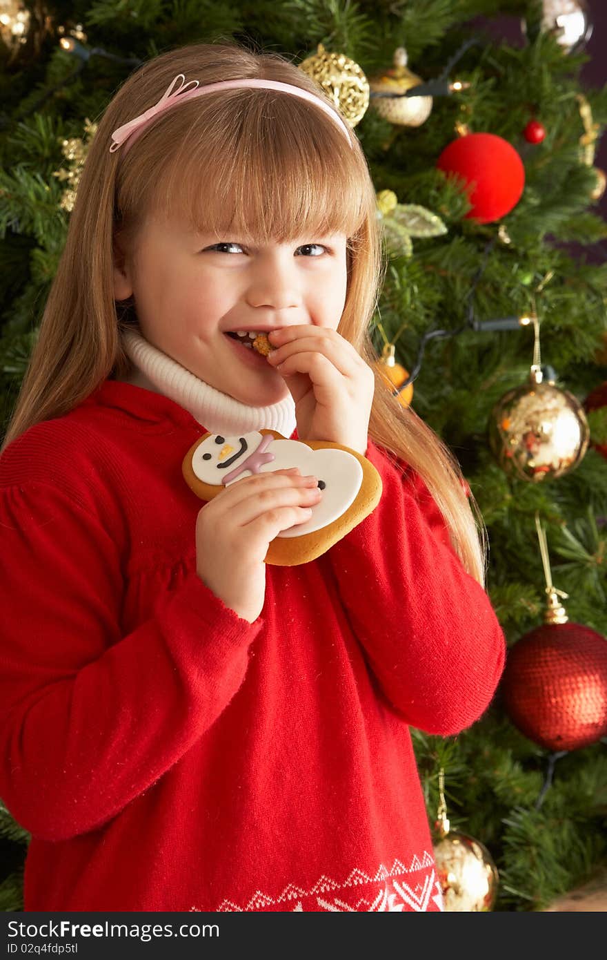 Girl Eating Cookie In Front Of Christmas Tree